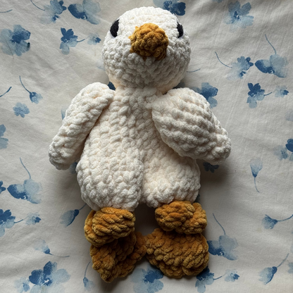 Crocheted goose snuggles with embroidered eyes on a floral-patterned fabric background