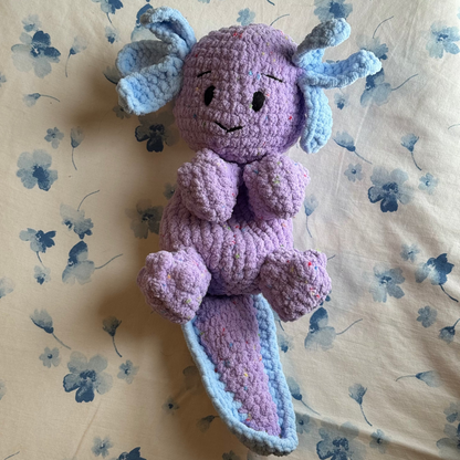 Crocheted purple creature with blue accents on a floral-patterned surface